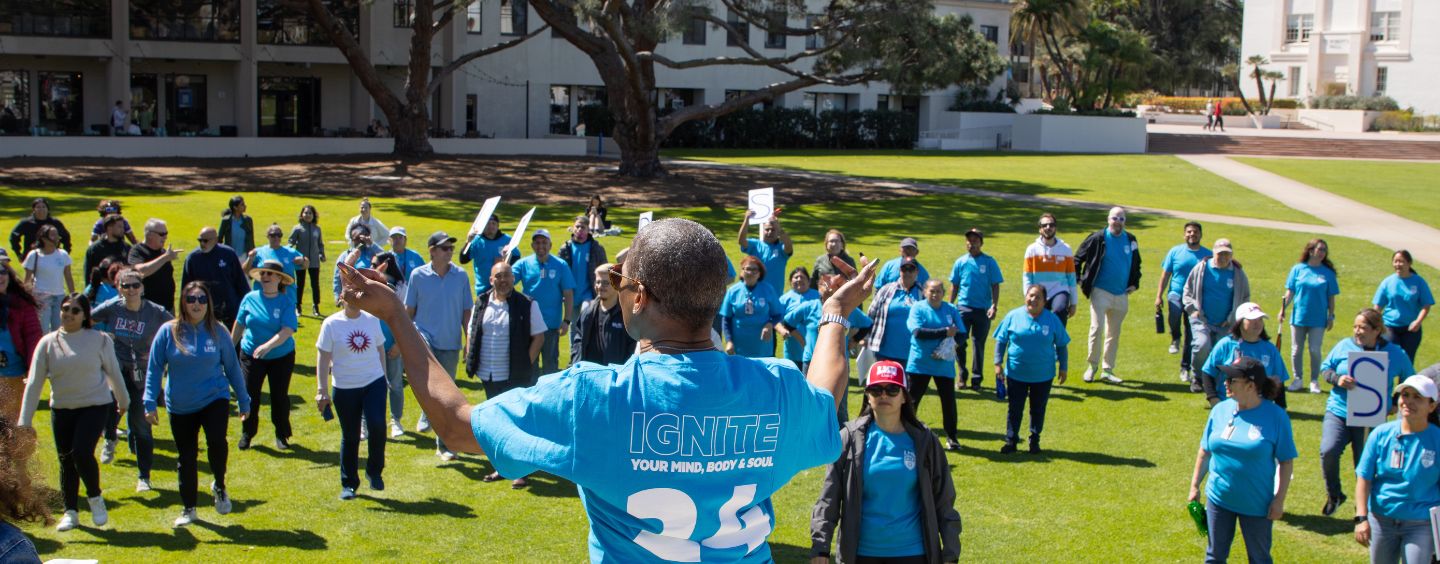 A staff member leading a large exercise group in Sunken Garden with words on her LMU branded shirt saying ignite your mind body and soul